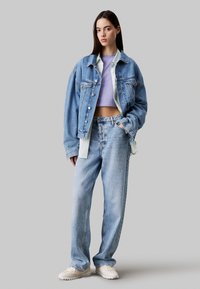 Chaqueta de mezclilla azul claro con botones plateados, camiseta blanca, top corto morado, y jeans de corte relajado. Zapatillas blancas completan el look.