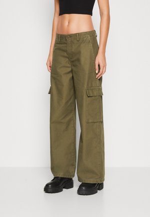 Slim-waist model wearing olive green wide-leg cargo pants with large side pockets and black chunky platform shoes.