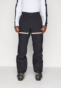 Fekete vízálló hó nadrág, tapered fazonnal, két vízszintes bézs cipzáras zsebbel és megerősített szegélyekkel a tartósság érdekében.