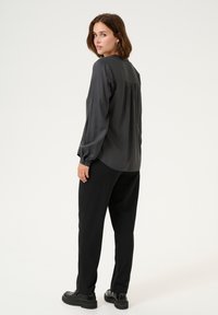 Grijze blouse met lange mouwen in een ontspannen pasvorm, met plooidetail op de rug, gecombineerd met zwarte tapered broek en stevige zwarte laarzen.