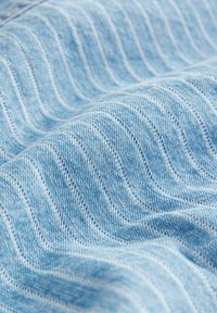 Denim azul claro con un patrón de ondas texturizadas. La tela presenta líneas de costura finas, creando un sutil contraste visual.