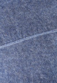 Texturierter blauer Stoff mit einer Mischung aus helleren und dunkleren Fäden, der ein geripptes Muster aufweist und eine sichtbare Naht über den Stoff verläuft.