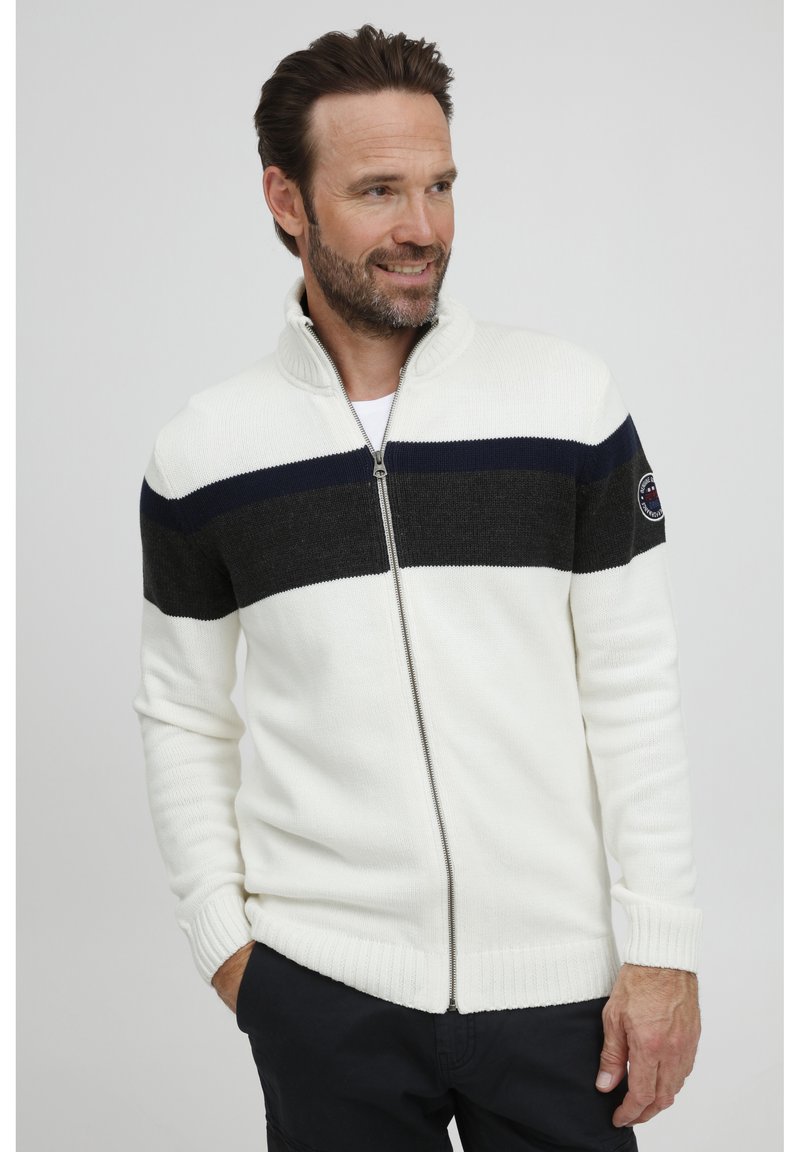 Sudadera con cremallera en crema con rayas horizontales en azul marino y gris oscuro. Presenta un cuello alto, puños acanalados y un parche con el logotipo en la manga.