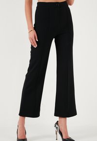 Black wide-leg pants made from smooth fabric with a front button closure, featuring deep side pockets and vertical seam details.