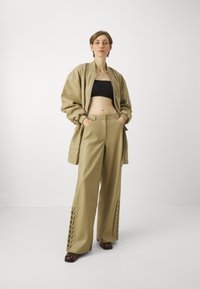 khaki bomber bunda přes černý crop top, doplněná širokými kalhotami s šněrováním na lemu a hladkou texturou látky.