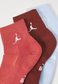 Tres pares de calcetines tobilleros en rojo, marrón y azul claro, con textura acanalada y el logo Jumpman blanco en la parte delantera.