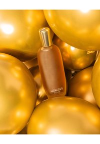 Bouteille en verre ambre étiquetée "ELIXIR AROMATIQUES" au milieu de ballons dorés avec une texture lisse et brillante, reflétant la lumière pour un effet lumineux.