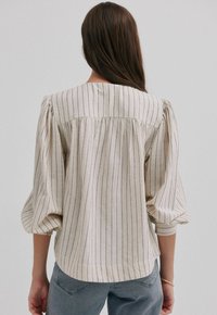 Gestreept, lichtgewicht, crèmekleurig shirt met pofmouwen en een gegatherde achterkant. Heeft verticale marineblauwe strepen en een ontspannen pasvorm.