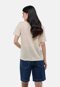 T-shirt en lin beige à manches courtes, coupe légèrement ample, assorti à un short bermuda en denim foncé, présentant un design simple et un look décontracté.