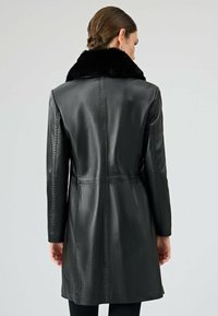 Czarna skórzana kurtka z kołnierzem z sztucznego futra, o dopasowanym kroju, długich rękawach i długości średniej. Gładka faktura z widocznymi szwami.