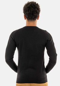 Maglione nero a maniche lunghe con un design aderente, texture liscia e polsini e orlo a coste, visto da dietro.