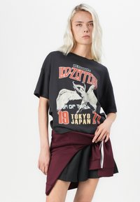 Black oversized t-shirt featuring a vintage Led Zeppelin concert graphic, paired with a maroon layered skirt and a black pleated detail.