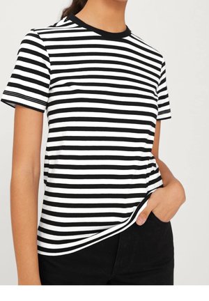 Personne portant un t-shirt à manches courtes rayé horizontalement noir et blanc, avec une main dans la poche d'un pantalon noir.