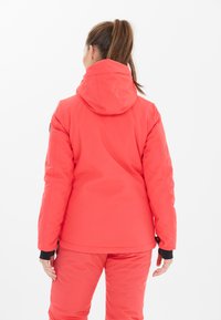 Rote isolierte Jacke mit Kapuze, die eine glatte Textur hat und schwarze Akzente an den Ärmeln aufweist, von hinten betrachtet, passend zu einer Hose im gleichen Design.