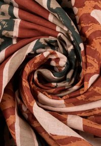 Tessuto di cotone con un motivo vorticoso in tonalità terrose di ruggine, beige e verde, arricchito da forme astratte e strisce a contrasto.