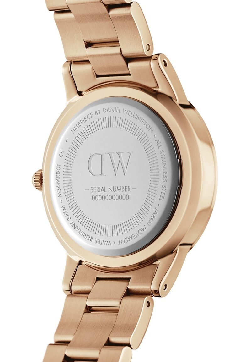 Montre en acier inoxydable rose doré avec le nom de la marque et le numéro de série gravés à l'arrière, offrant un boîtier lisse et rond ainsi qu'un bracelet à maillons.