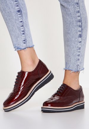 Burgunderrote Lackleder-Schnürschuhe mit sleekem Design, kontrastierender weißer und schwarzer Sohle sowie dekorativen Nähten.