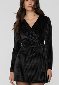Czarna welurowa sukienka kopertowa z długimi rękawami, z głębokim dekoltem w kształcie litery V, subtelnym wzorem diamentowym i wiązaniem w talii. Gładka tekstura.