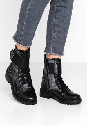 Zwart-grijze veterenkelboots met zijrits, met studs versierd en een band over de voorkant, gedragen met versleten grijze jeans.