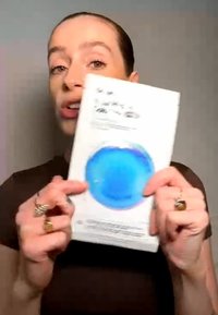 Persona sosteniendo y mostrando un libro con una cubierta blanca que presenta un gran diseño circular azul en el centro.