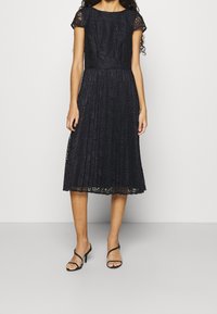 Robe en dentelle navy avec des manches courtes, un corsage ajusté et une jupe évasée plissée. Présente des motifs en dentelle élaborés et une longueur au genou.