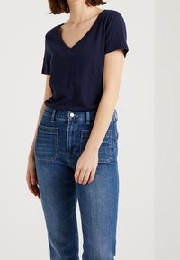 Camiseta de cuello en V de color navy hecha de algodón, combinada con jeans de tiro alto de color azul oscuro que presentan grandes bolsillos frontales y una textura de denim desgastado.