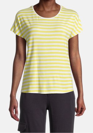 Personne portant un t-shirt jaune et blanc à rayures horizontales à manches courtes et un pantalon noir avec une poche latérale, debout, les bras détendus.