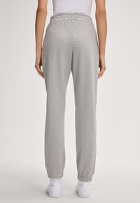 Grau Sweatpants mit schmal zulaufendem Bein, elastischem Bündchen und Bündchen an den Knöcheln. Hergestellt aus einem weichen, atmungsaktiven Stoff, von hinten betrachtet.