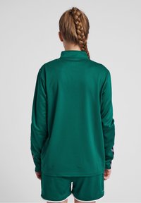 Jersey deportivo de poliéster verde de manga larga con un patrón texturizado, que cuenta con un cuello y acentos en gris en contraste en las mangas.