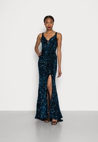 Kimalle teal-sequined gown, jossa on tiukka yläosa, syvä V-kaula-aukko ja reiteen yltävä halkio. Suunniteltu spagettiolkaimilla ja leveällä helmalla.