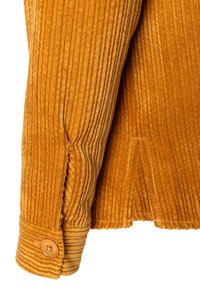 Senffarbenes Cord-Jackett mit vertikal gerippter Textur, fertigem Bund und runder Knopfdetails. Saubere Nähte an der Naht.