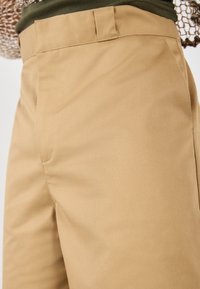 Pantalon en coton beige avec une texture lisse, présentant une coupe droite, des poches latérales et un design de taille épuré.