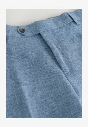 Hellblauer Denimstoff mit glatter Textur, ausgestattet mit einer zentralen Falte und einem einzelnen Metallknopf am Bund zum Verschließen.