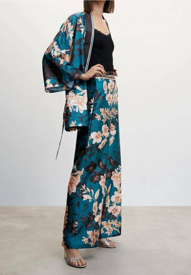 Kimono floral bleu sarcelle avec des fleurs roses et noires, tissu léger, devant ouvert, associé à un pantalon large assorti, sandales à talons transparents.