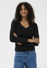 Čierny kardigán s výstrihom do V, dlhými rukávmi a zapínaním na gombíky, kombinovaný s modrými džínsami. Hladká textura a priliehavý strih.