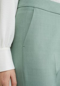 Pantalones ajustados de color verde claro confeccionados con una tela suave de sutil textura. Presenta bolsillos laterales y una cintura ajustada.