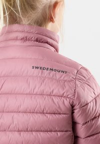 Lyserød pufferjakke med quiltet design, der har høj krave og sort "SWEDEMOUNT" logo på ryggen. Glat, letvægts materiale.