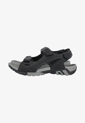 Sandales noires en synthétique avec des sangles réglables, des accents gris, une semelle en caoutchouc texturé, et un design sportif, featuring un bout ouvert et un talon ouvert.
