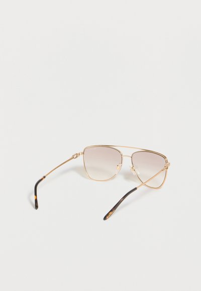 Αviator γυαλιά ηλίου με χρυσό πλαίσιο, καφέ φακούς με διαβαθμισμένο χρώμα και μύτες βραχίονα με σχέδιο χελώνας σε λευκό φόντο.