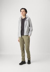 Vaaleanharmaa fleece-takki, jossa on kaulus, musta t-paita sen alla, oliivinvihreät housut ja mustat jalkineet. Yksinkertainen ja toiminnallinen ulkoiluasu.