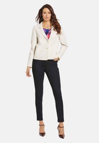 Ivoor blazer met een aansluitend ontwerp, enkele knoopsluiting en twee voorzakken, gecombineerd met aansluitende marineblauwe broeken en bordeauxrode hakken.