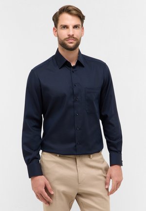 Navy blauwe button-up shirt van gladde stof, met een borstzak, lange mouwen en knoopmanchetten. Gepaard met beige broeken.