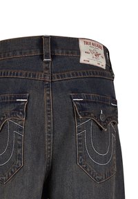 Ciemnoniebieskie dżinsy o wysokim stanie, z kontrastującymi pomarańczowymi szwami i charakterystycznymi podwójnymi tylnymi kieszeniami z białymi wzorami szycia.