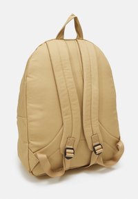 Beige stoffen rugzak met een ronde vorm, gewatteerde schouderbanden en een handvat aan de bovenkant. Voorzien van verstelbare gespen en een gestructureerd oppervlak.