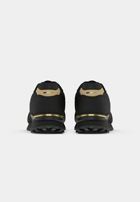 Sapatilhas atléticas pretas com detalhes em dourado. Parte superior em tecido texturizado, colarinho acolchoado e sola preta robusta com padrão de tração.
