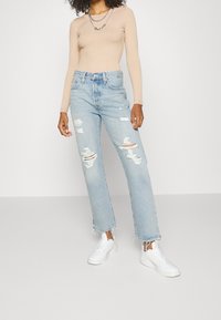 Ljusblå rivna jeans med rakt ben, fransad nederkant och lös passform, i kombination med en beige ribbad långärmad topp och vita sneakers.