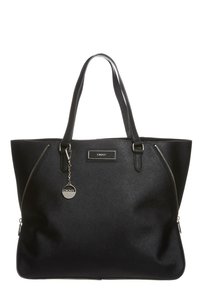 Sac cabas noir DKNY avec doubles poignées, écusson logo à l’avant, détails zippés sur les côtés et breloque ronde en métal avec logo suspendue à une poignée.