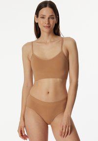 Béžový bralette s tenkými ramínky a bezešvým designem, doplněný o odpovídající džínové kalhotky s vysokým pasem. Měkká, elastická tkanina, minimalistický styl.