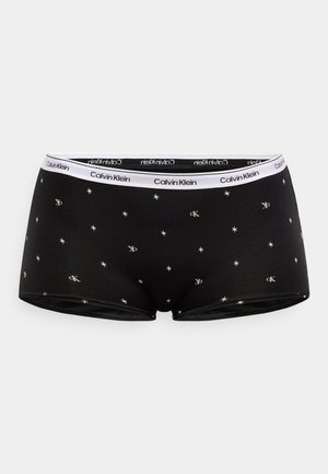 Black boxer shorts featuring a star and 'CK' pattern in beige. Elastic waistband with a white Calvin Klein logo. Soft, stretchy material.