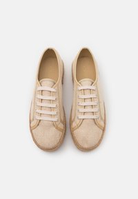 Zapatillas de malla beige con cordones color crema, suelas de goma marrón y tejido texturizado; presentan detalles de costura y un diseño de punta redondeada.